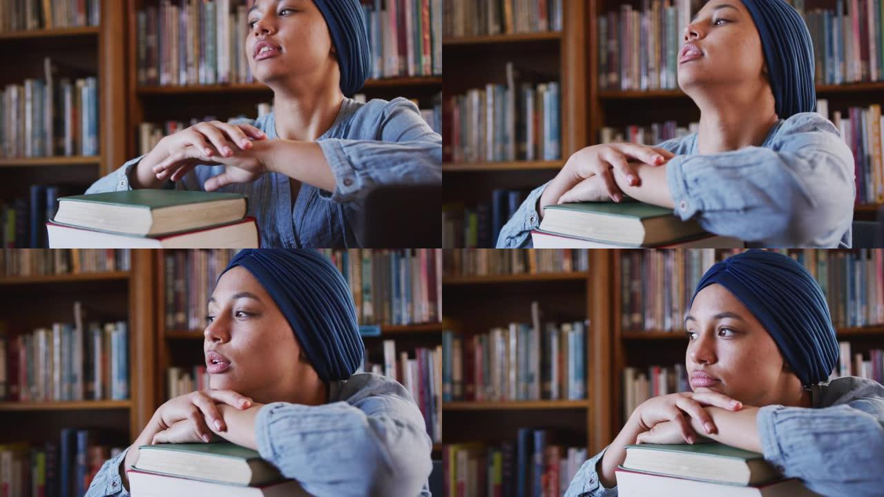 戴蓝色头巾的亚裔女学生坐著靠著一堆书思考