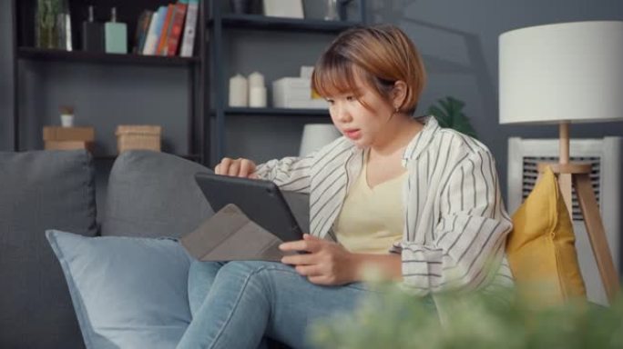 自由亚洲女士休闲服使用平板电脑在线学习在家里的客厅。