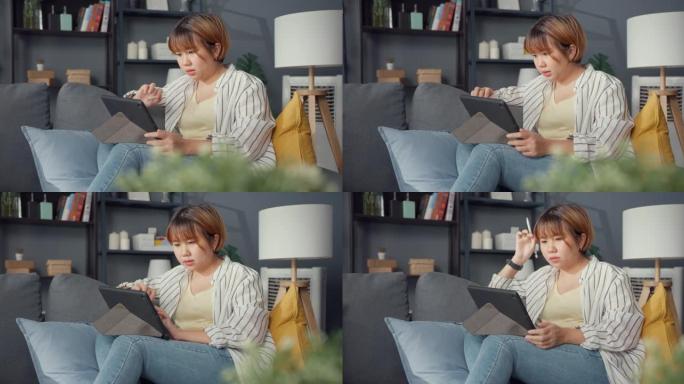 自由亚洲女士休闲服使用平板电脑在线学习在家里的客厅。