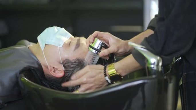 戴着保护面罩的亚裔华人男子在美发沙龙里闭着眼睛躺着洗头
