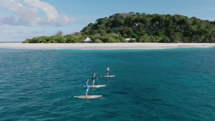 塞舌尔库辛岛周围的三个人在站立的桨板上玩耍的鸟瞰图