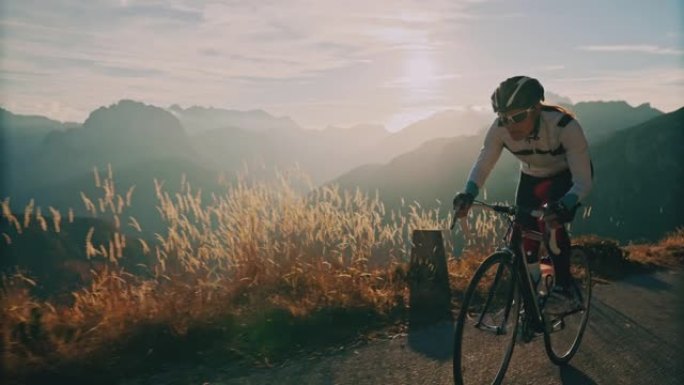 女自行车手在日出时在阳光明媚的山路上坡骑行