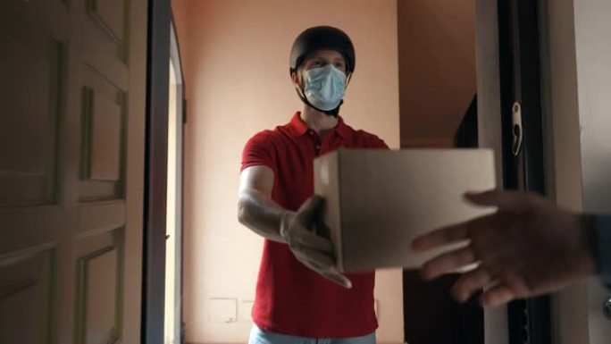 一位年轻的邮递员快递员戴着防护口罩和手套，正在安全地将包裹直接运送到客户家中。快递，送货上门，电子商