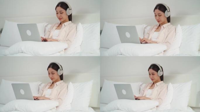 亚洲女商人使用技术笔记本电脑和耳机在床上进行在线学习