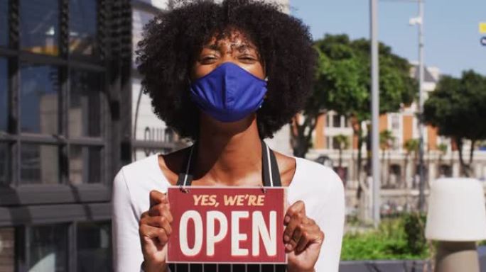 非裔美国女咖啡馆工作人员戴着面罩，展示着开放的标牌