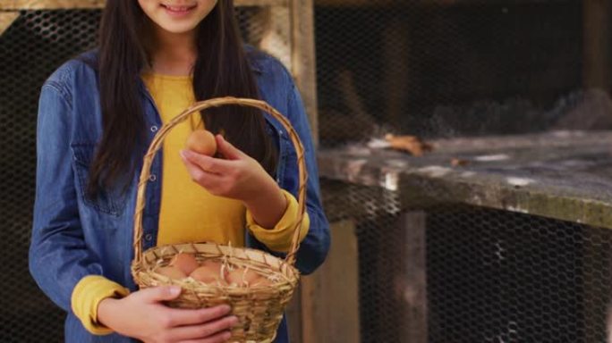 微笑的亚洲女孩，带着一篮子鸡蛋站在花园里的鸡舍旁