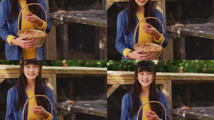 微笑的亚洲女孩，带着一篮子鸡蛋站在花园里的鸡舍旁