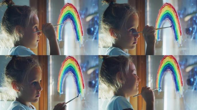 一个可爱的小创意快乐微笑的学龄前女孩画家的真实镜头正在家里厨房的窗户玻璃上画彩虹