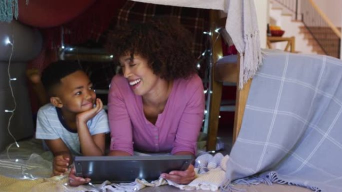 快乐的非洲裔美国母亲和儿子躺在用平板电脑制成的毯子房子里