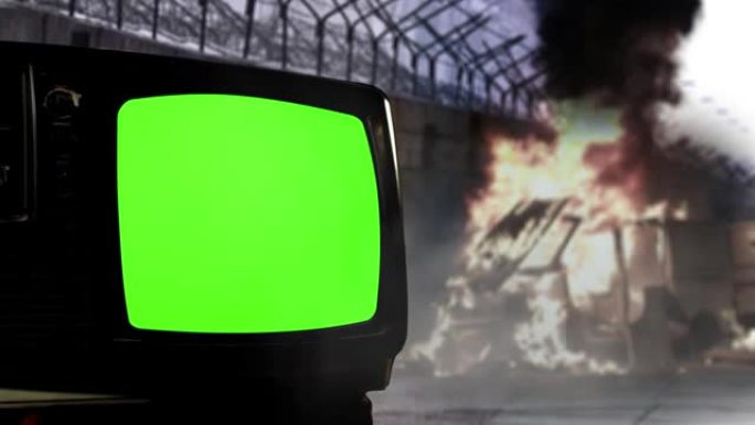 街上的骚乱和旧电视绿屏。火焰从燃烧的货车附近升起，墙壁上有带刺的铁丝网和带有绿色屏幕的复古电视机。多