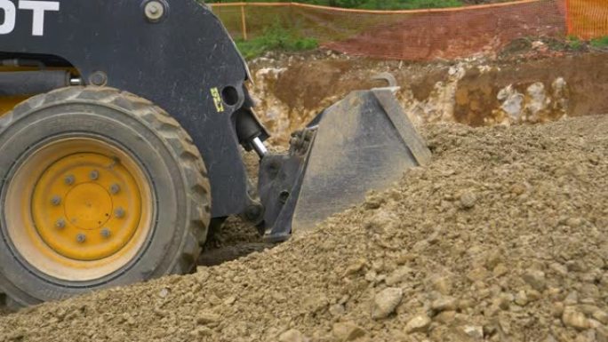 特写: 挖掘机向前行驶，铲起装满湿岩石的水桶。