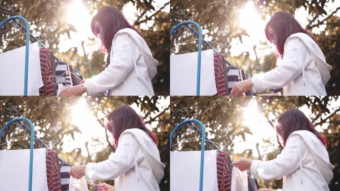 活跃的高级妇女戴着防护口罩，将洗过的衣服挂在她的房子前