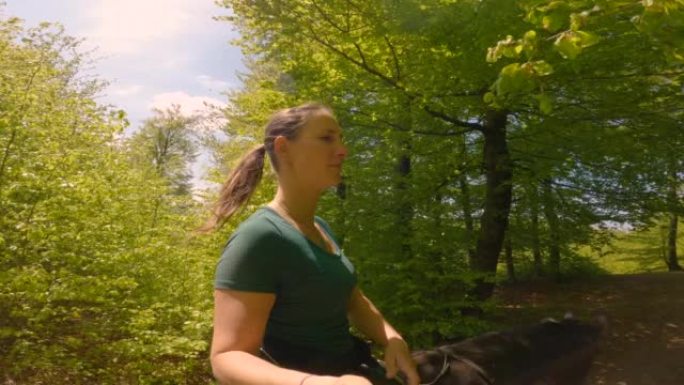 肖像: 年轻的女性在森林小径上骑马穿过绿树