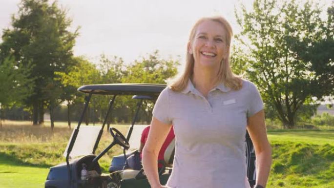 微笑的成熟女高尔夫球手站在高尔夫球场上的童车旁边的肖像