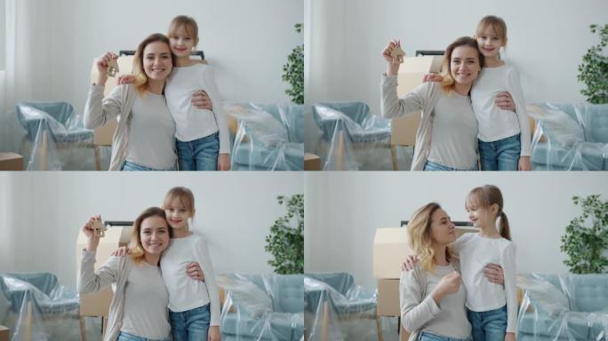 幸福的年轻母亲和小女儿微笑的肖像在室内拿着房子的钥匙