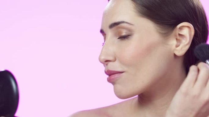 4k视频片段，一位迷人的年轻女子在粉红色的工作室背景下用刷子化妆