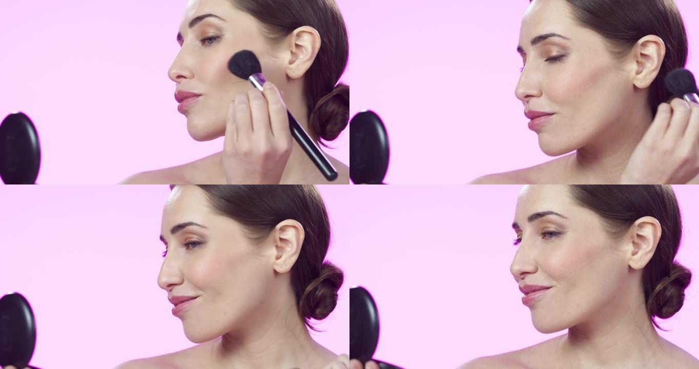 4k视频片段，一位迷人的年轻女子在粉红色的工作室背景下用刷子化妆