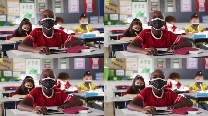 非裔美国男孩坐在学校的课桌上戴着口罩