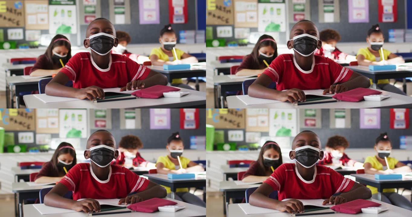 非裔美国男孩坐在学校的课桌上戴着口罩