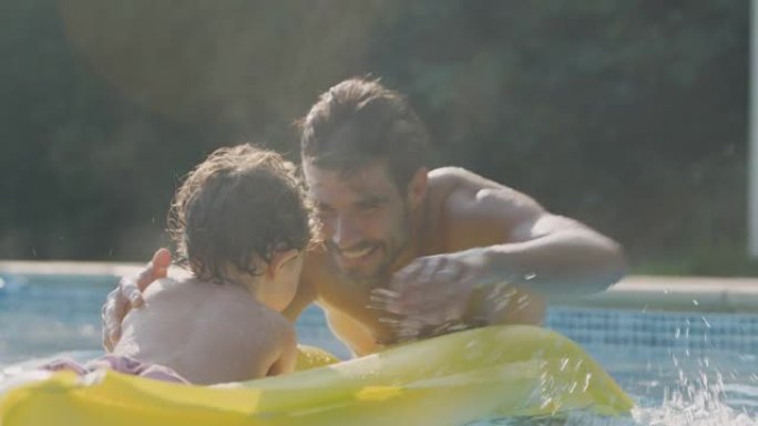 父子俩暑假在室外游泳池的充气充气床上玩耍