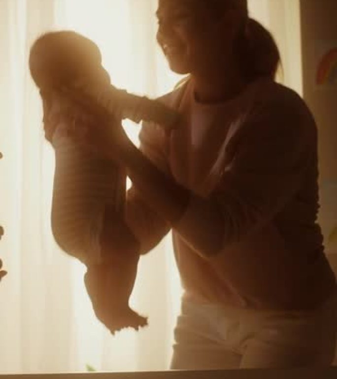 母亲在黑暗的房间里从婴儿床里捡起一个可爱的新生男婴的垂直格式视频。妈妈从床上抱起幼儿。童年、新生活、