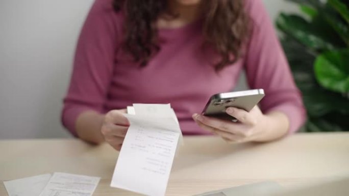 女人拿着智能手机的收据，在家计算账单，在线支付
