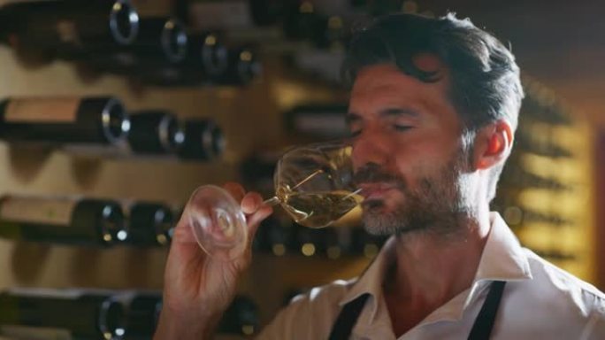 成功的男性侍酒师的真实照片正在品尝一种风味，并检查倒入酒窖透明玻璃杯中的白葡萄酒质量。