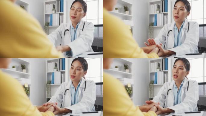 穿着白色医疗制服的年轻亚洲女医生在诊所或医院办公室坐在办公桌前的会议上讨论触摸女孩病人的肩膀。心理帮