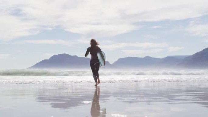 混血女子从海滩跑到海边的后视图携带冲浪板