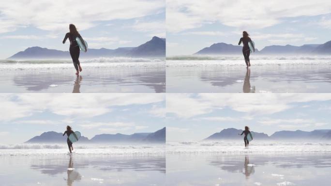 混血女子从海滩跑到海边的后视图携带冲浪板