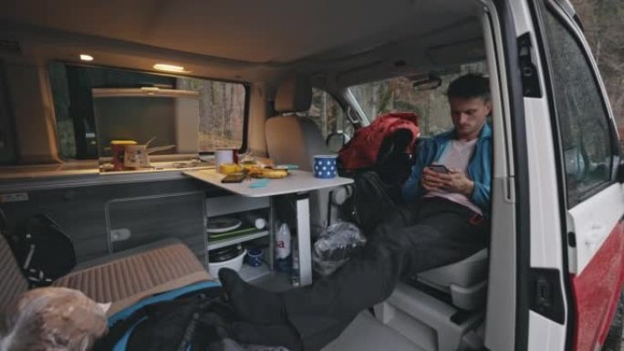 棕色短发的男人坐在货车上，伸着腿，用智能手机