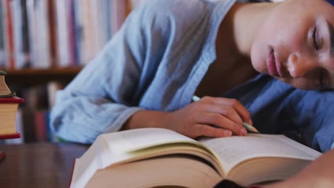 穿着蓝色头巾的亚洲女学生坐在打开书本的书桌前睡觉