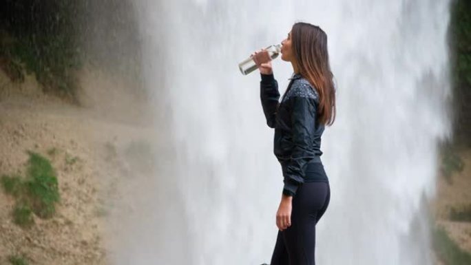 年轻女运动员在瀑布前喝水