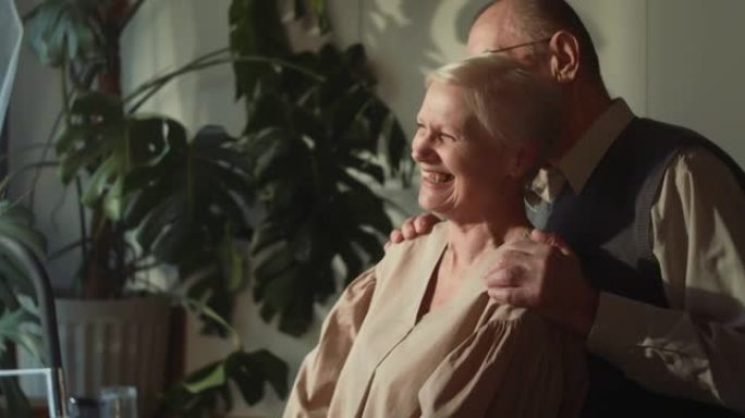 成功的婚姻。幸福可爱的浪漫60年代高级丈夫拥抱白发妻子在舒适的家中微笑的肖像。