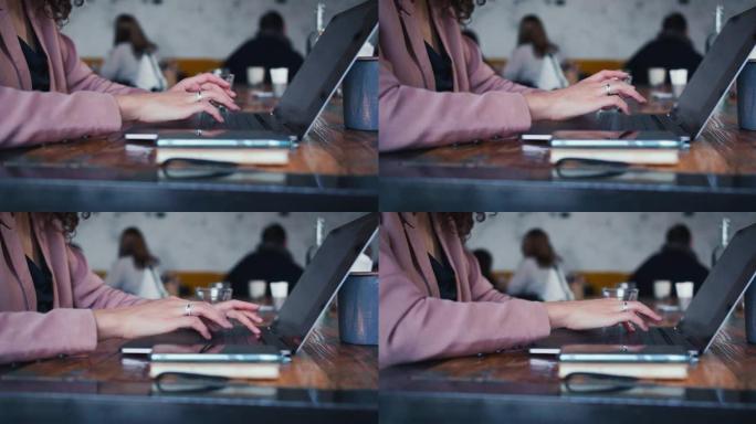 时髦的女商人用笔记本电脑打字信息的特写手，在时髦的咖啡馆木桌上在线工作。
