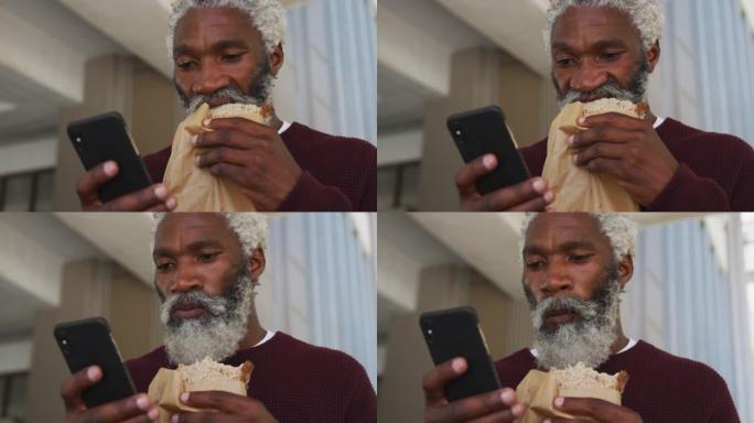 非裔美国人高级男子在公司公园吃零食并使用智能手机