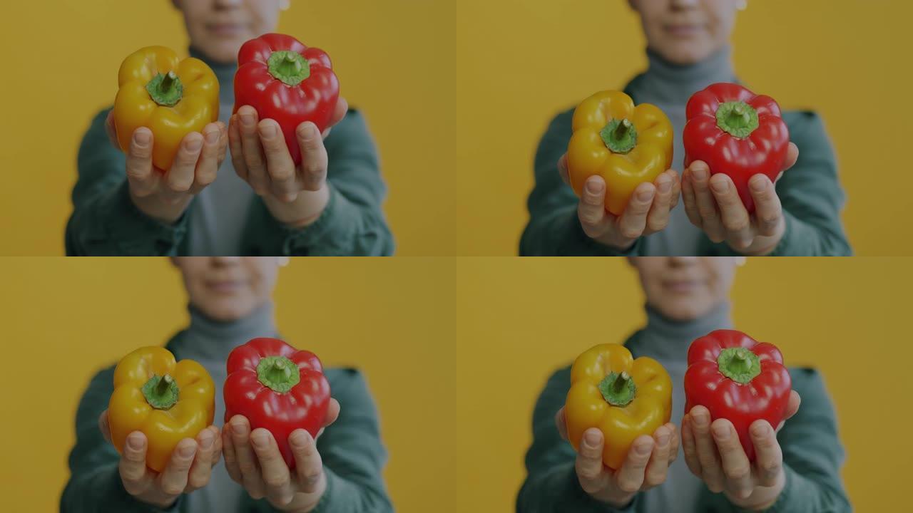 女性双手拿着新鲜的胡椒将蔬菜移到相机上，而女性在黄色背景上模糊