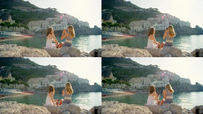 快乐的朋友坐在海边用手机拍照。两名妇女在假日用智能手机拍照