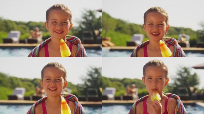 暑假与女孩一起在游泳池边缘吃冰棍的家庭看着相机