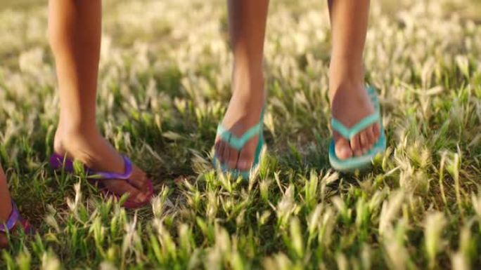 孩子们，夏天和脚跳着人字拖在草地上，一起度假，娱乐和童年。自由，假期和孩子们在阳光下快乐地跳上草坪，