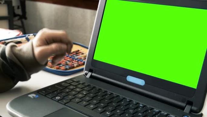 十几岁的男孩在绿屏笔记本电脑上打字。放大。