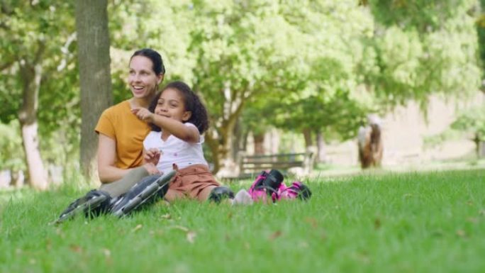 快乐的慈爱的母亲和她可爱的收养的小孩在公园的草地上放松和交谈。微笑的女人和女儿在花园里度过的家庭日，