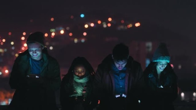 夜晚，屋顶和游戏朋友与智能手机在线视频游戏移动应用程序在黑暗中与bokeh城市之光。社交媒体快乐，z