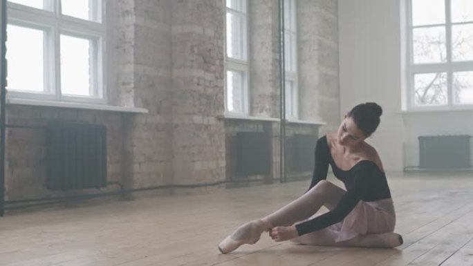 优雅的芭蕾舞女演员在地板上系脚鞋