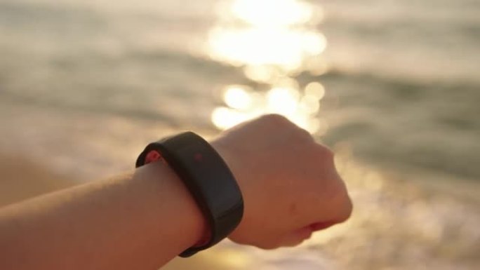 女人使用智能手表检查心率，日落时在海滩上使用智能手表