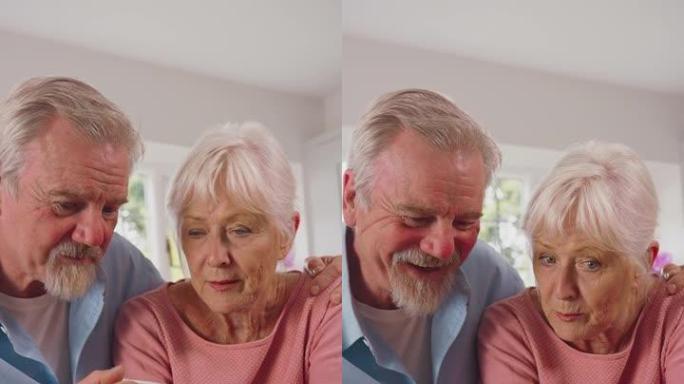 退休的高级夫妇在家里用数字平板电脑在线厨房购物或预订假期的垂直视频-慢动作拍摄