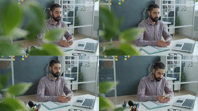 工作场所使用智能手机触摸屏的快乐阿拉伯男子在工作中享受社交媒体