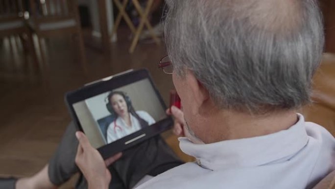 年迈的爷爷拿着一瓶药咨询医生，用平板电脑作为视频通话，以缩小他们之间的距离，减少传播感染的机会