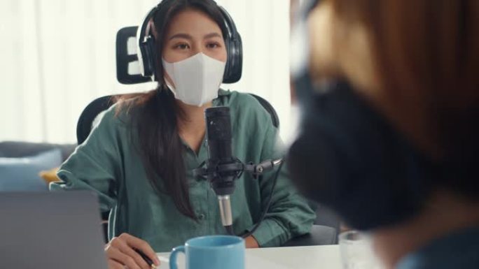 亚洲女孩电台主持人录音播客使用麦克风戴耳机采访嘉宾内容戴口罩保护病毒谈话在她的房间里听。