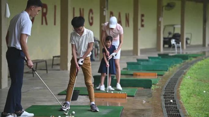 亚洲华裔年轻夫妇高尔夫球手教他们的孩子在高尔夫练习场打高尔夫球